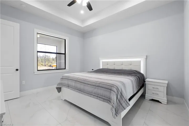 Spacious room featuring tray ceilings with recessed lighting, large format tile flooring, and a modern ceiling fan