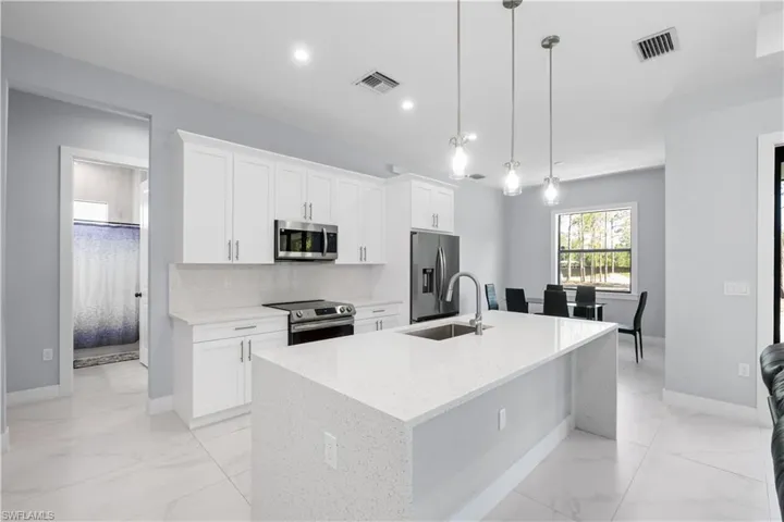 Open-concept kitchen featuring an expansive island with an undermount sink, white shaker cabinetry, stainless steel appliances, and large format white tile flooring