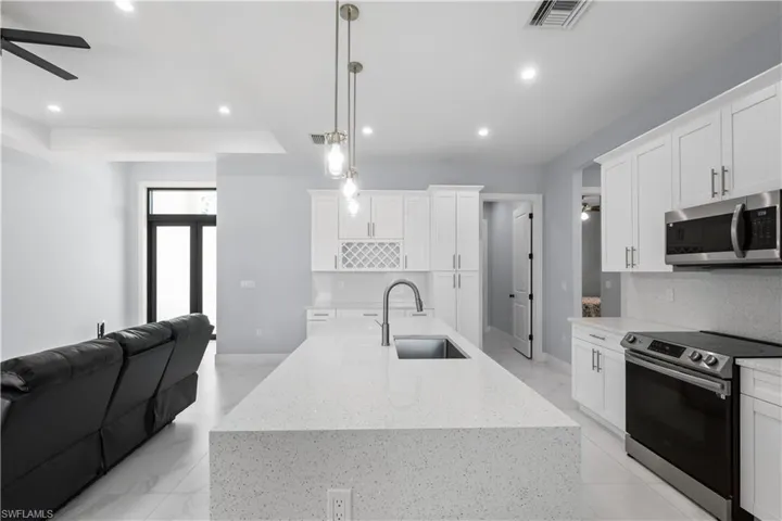 Open-concept kitchen featuring a large island with an undermount sink, pendant lighting, white cabinetry, stainless steel appliances, and tile flooring