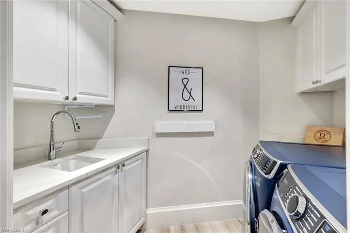 Clothes washing area with sink, light hardwood / wood-style floors, separate washer and dryer, and cabinets