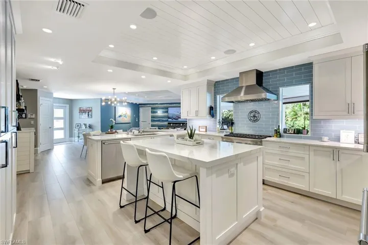 Kitchen featuring white cabinets, backsplash, a raised ceiling, a kitchen island, and wall chimney exhaust hood