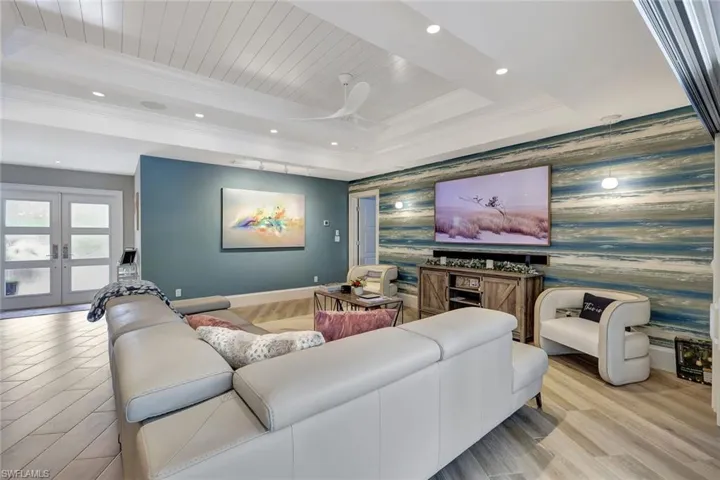 Home theater room featuring french doors, a raised ceiling, ornamental molding, and light wood-type flooring