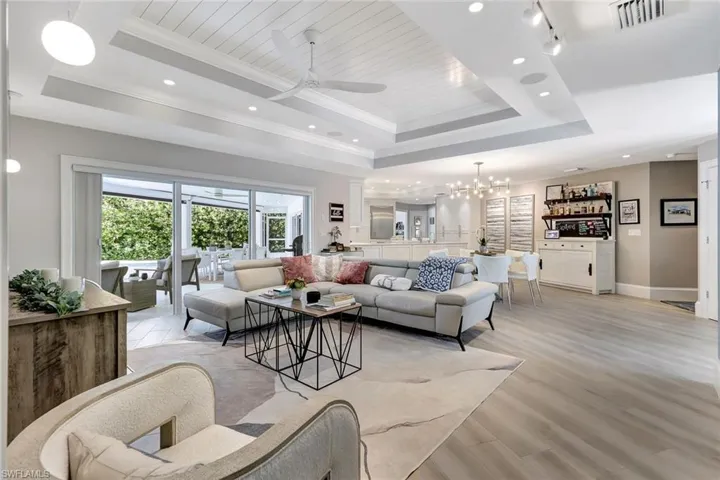 Living room featuring light hardwood / wood-style flooring, a tray ceiling, ceiling fan with notable chandelier, and crown molding