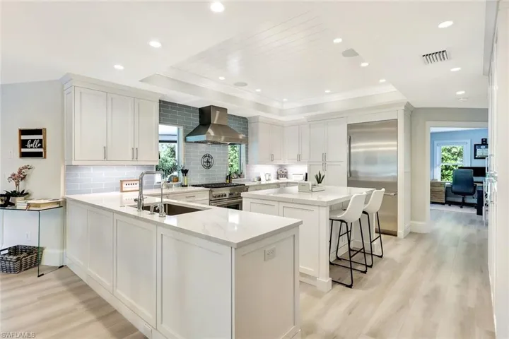Kitchen featuring wall chimney range hood, high quality appliances, light hardwood / wood-style flooring, kitchen peninsula, and a center island