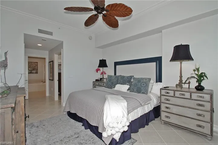 Bedroom with light tile patterned floors, ornamental molding, ensuite bathroom, and a ceiling fan