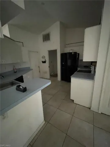 Kitchen featuring black refrigerator, light tile patterned floors, kitchen peninsula, sink, and white cabinets