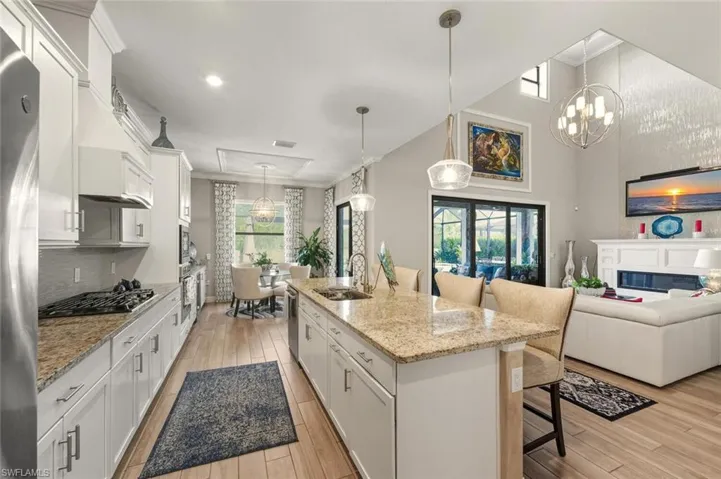 Kitchen with a kitchen bar, white cabinetry, hanging light fixtures, light stone counters, and a glass covered fireplace