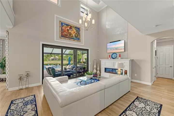 Living room featuring crown molding, light wood-type flooring, a glass covered fireplace, a high ceiling, and arched walkways