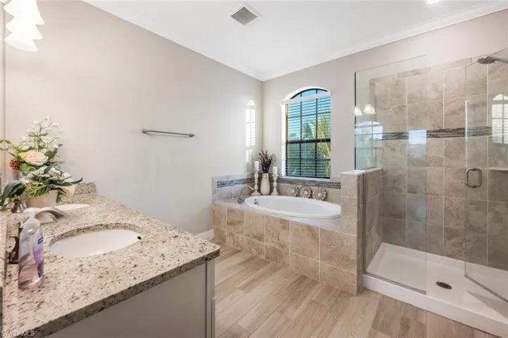 Full bathroom featuring a bath, ornamental molding, double vanity, a shower stall, and light wood-style floors