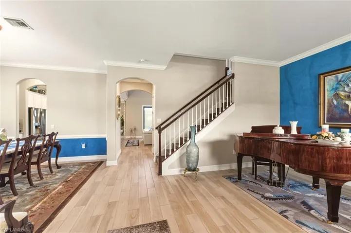Foyer entrance with light wood-style floors, arched walkways, ornamental molding, and stairway