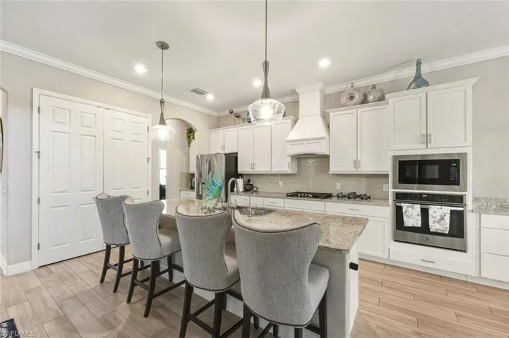 Kitchen featuring ornamental molding, appliances with stainless steel finishes, white cabinetry, backsplash, and light stone counters