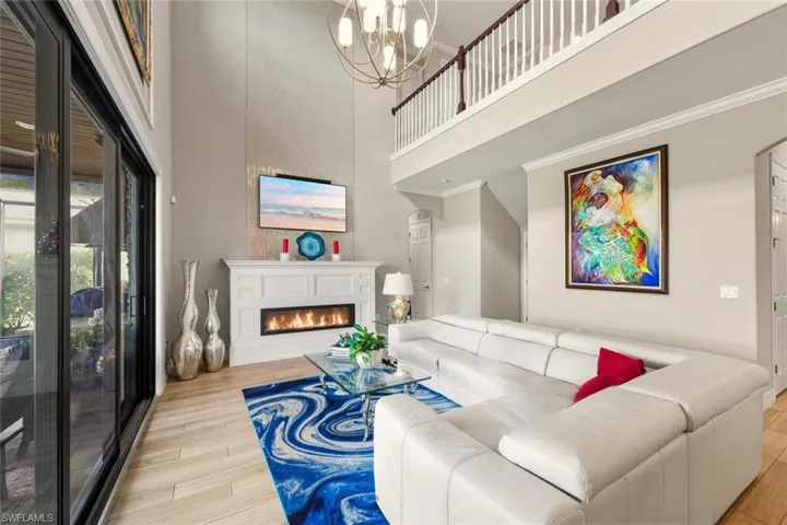 Living area with a warm lit fireplace, a towering ceiling, light wood finished floors, ornamental molding, and arched walkways