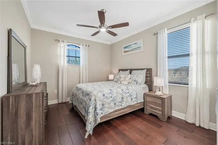 Bedroom with dark wood-style flooring, ceiling fan, and crown molding
