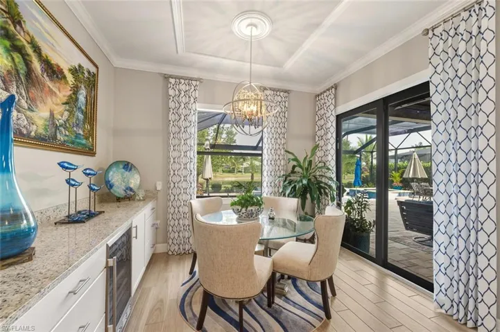 Dining space featuring light wood-style flooring, plenty of natural light, wine cooler, ornamental molding, and a chandelier