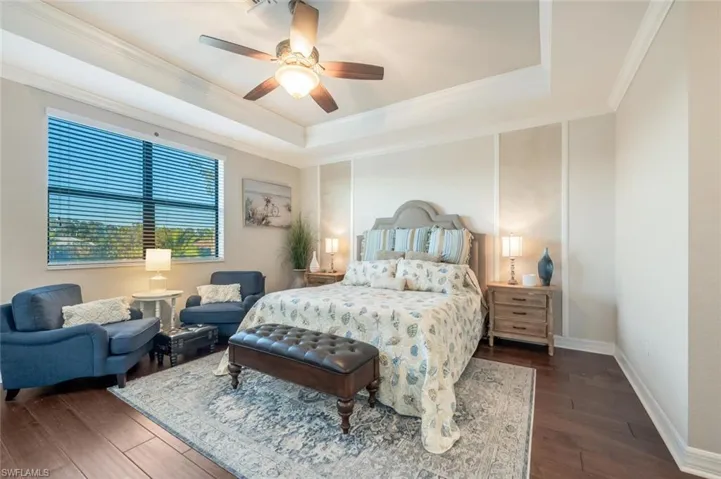 Bedroom with dark wood-style flooring, a tray ceiling, a ceiling fan, and ornamental molding