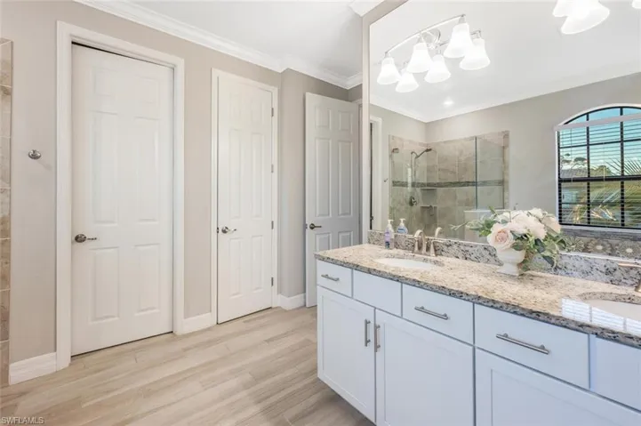 Bathroom with double vanity, a shower stall, light wood-type flooring, and ornamental molding