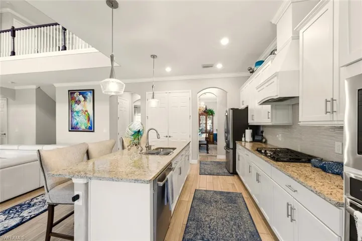 Kitchen with a breakfast bar area, arched walkways, light stone counters, ornamental molding, and white cabinets