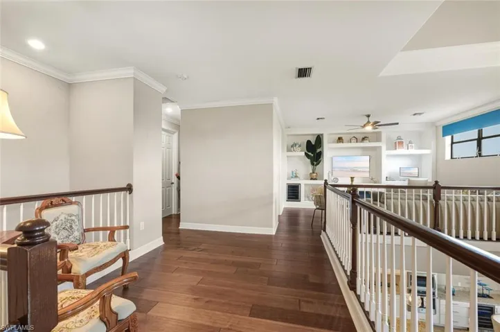 Hallway with an upstairs landing, dark wood-style flooring, ornamental molding, recessed lighting, and built in shelves