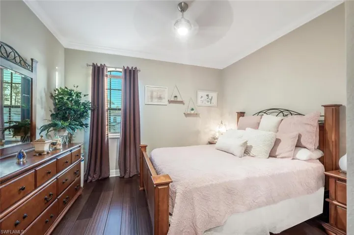Bedroom with ornamental molding, dark wood-type flooring, and ceiling fan