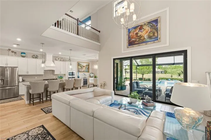 Living area featuring a chandelier, a high ceiling, light wood-style floors, beverage cooler, and recessed lighting