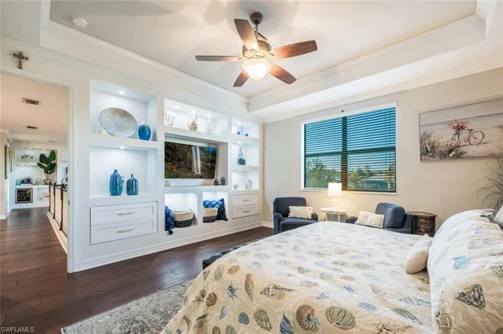 Bedroom with crown molding, dark wood-type flooring, a tray ceiling, and a ceiling fan