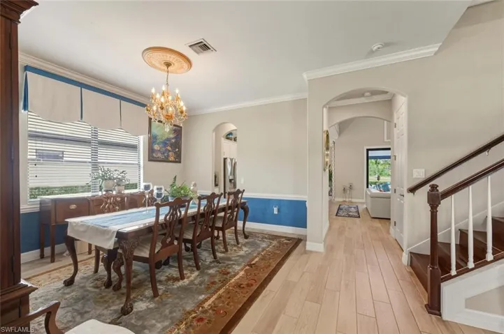 Dining room featuring light wood finished floors, arched walkways, crown molding, stairs, and a chandelier