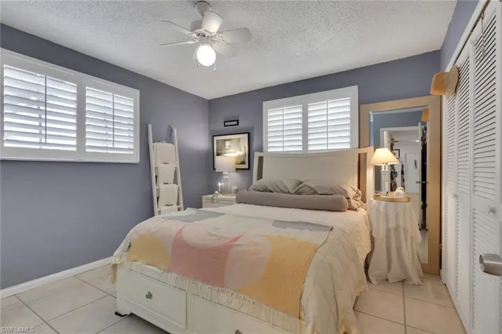 Bedroom with a closet, plantation shutters, a ceiling fan, and light tile patterned floors