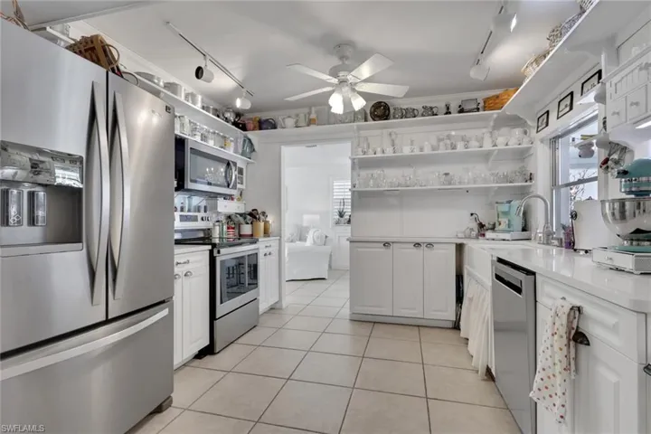Kitchen with open shelves, stainless steel appliances, white cabinetry and track lighting.