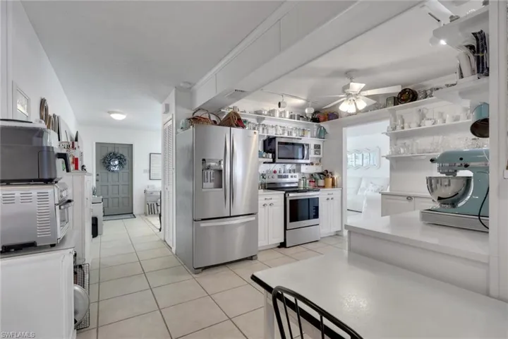 Kitchen with stainless steel appliances, white cabinetry, light countertops, open shelves, and track lighting