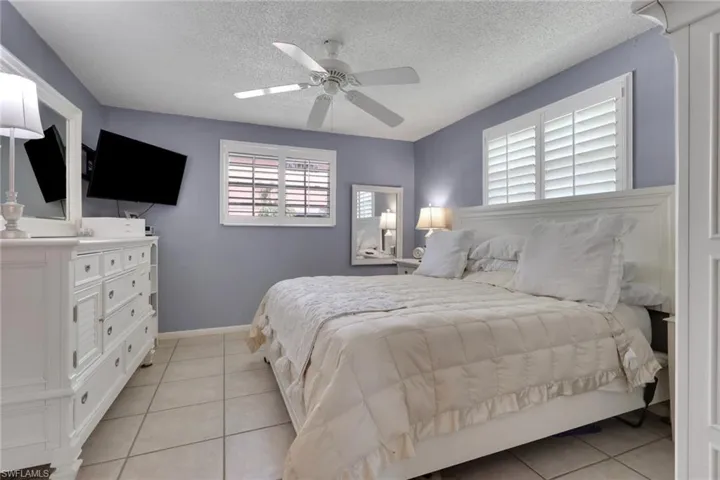 Bedroom featuring light tile patterned flooring, a ceiling fan, and plantation shutters; room shown with a king bed