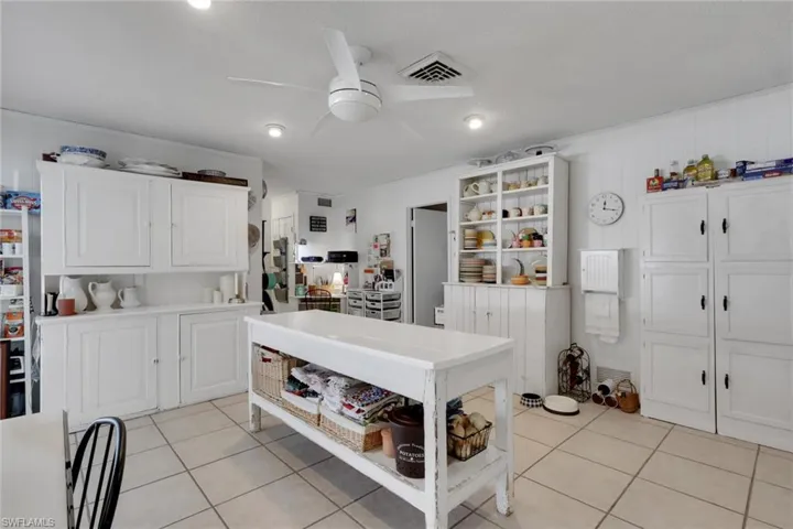 Kitchen featuring white cabinets for additional storage and pantry space, open shelves, light countertops, and light tile patterned floors; kitchen work station for prepping or serving