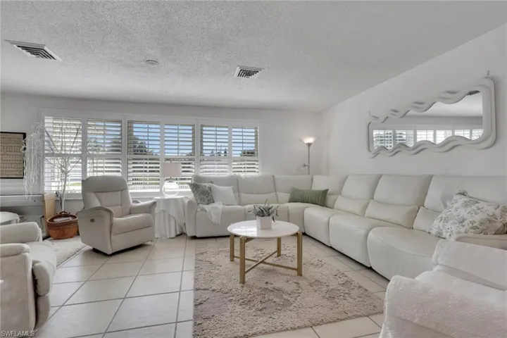 Living room with tile patterned floors and healthy amount of natural light coming through the open plantation shutters