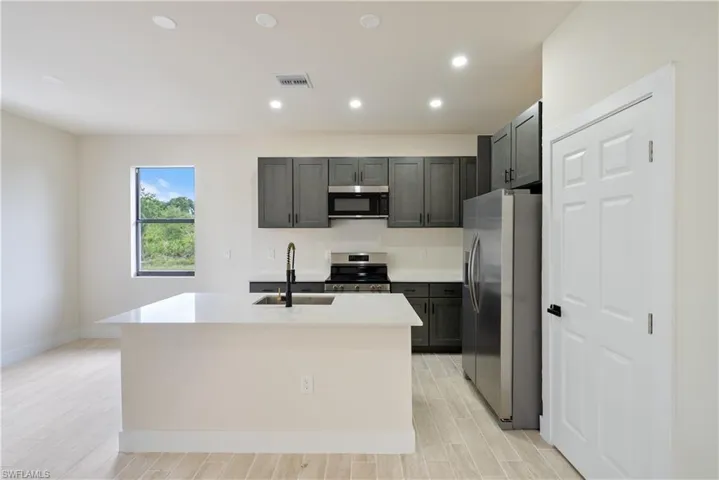 Kitchen featuring stainless steel appliances, wood finish floors, a center island with sink, light stone countertops, and recessed lighting