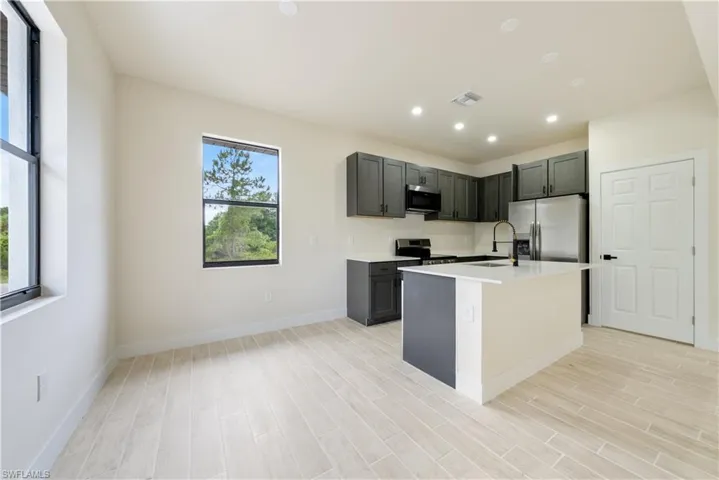 Kitchen with wood tiled floors, stainless steel appliances, an island with sink, recessed lighting, and light stone counters