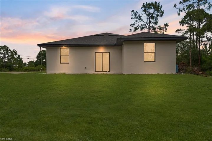 Back of house at dusk featuring a lawn, stucco siding, and roof with shingles