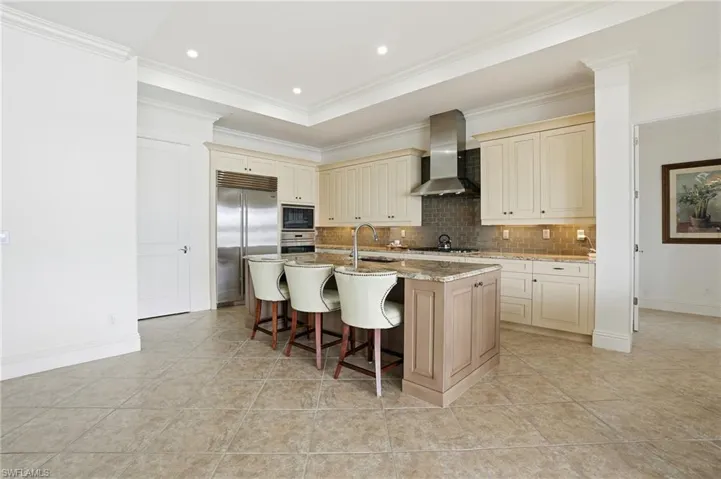 Kitchen with cream cabinets, a breakfast bar, light stone counters, built in appliances, and backsplash