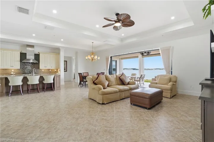 Living room featuring crown molding, a ceiling fan, a chandelier, light tile patterned floors, and recessed lighting