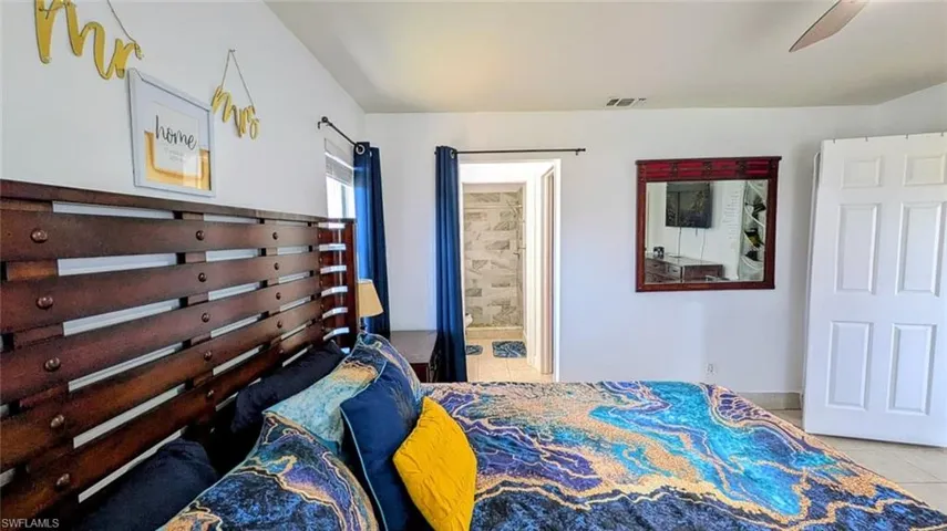 Bedroom featuring light tile patterned floors, ensuite bathroom, and ceiling fan
