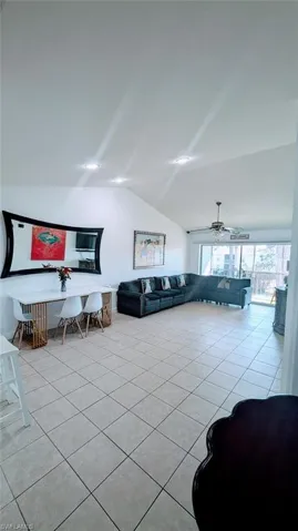 Living area with lofted ceiling, light tile patterned floors, and ceiling fan
