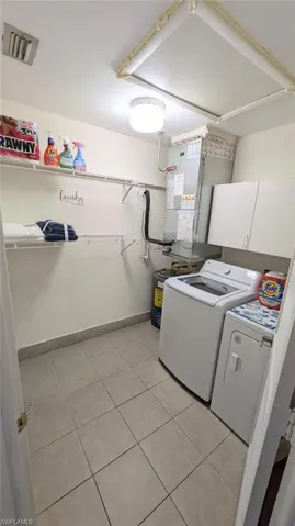 Laundry room featuring cabinet space, separate washer and dryer, heating unit, and light tile patterned floors