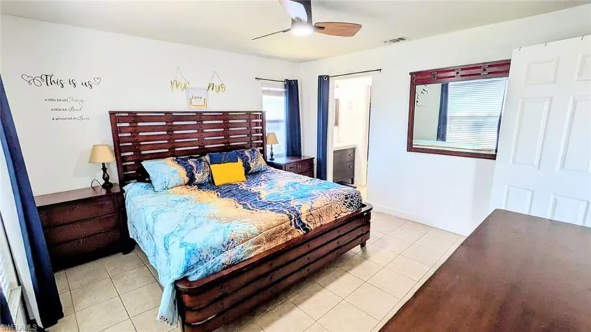 Bedroom featuring light tile patterned flooring, a ceiling fan, and ensuite bath