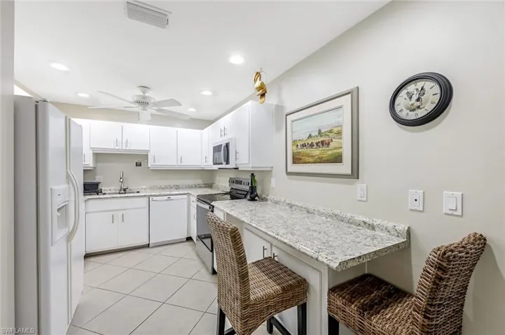 Kitchen featuring white appliances, white cabinets, a kitchen breakfast bar, light tile patterned flooring, and recessed lighting