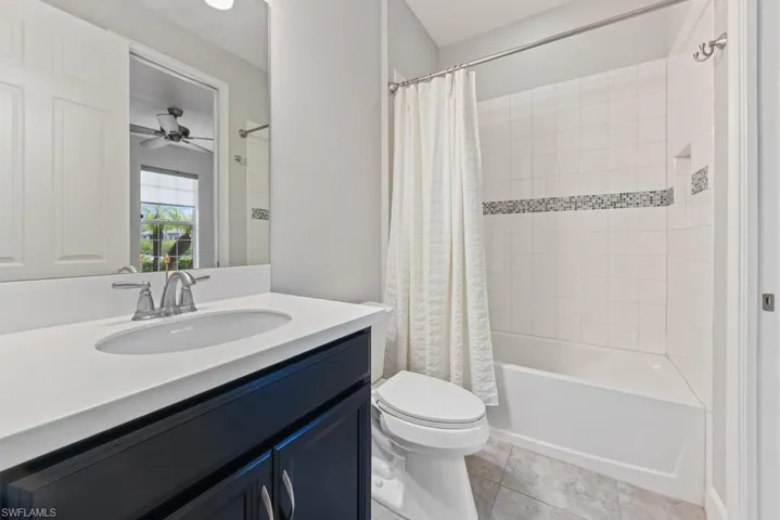 Full bathroom with vanity, tile patterned flooring, toilet, shower / bathtub combination with curtain, and ceiling fan