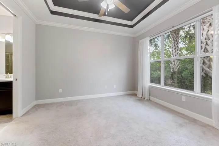 Carpeted Primary Bedroom with crown molding, ceiling fan, and a tray ceiling