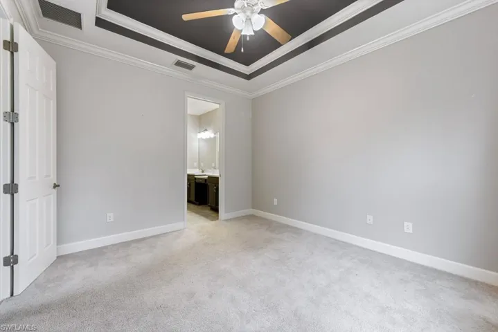 Primary bedroom with ceiling fan, a raised ceiling, light carpet, and ornamental molding