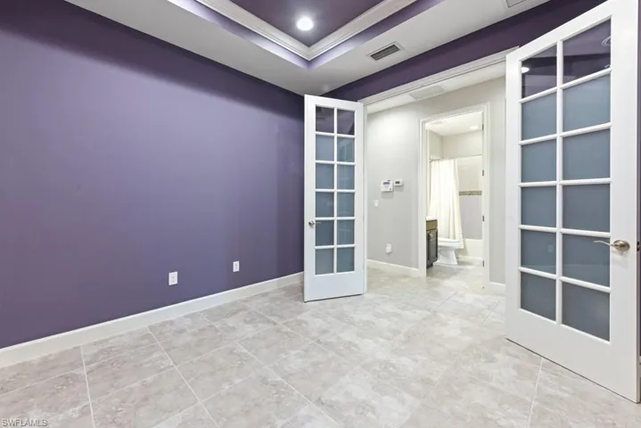 Tiled empty room with a tray ceiling, ornamental molding, and french doors