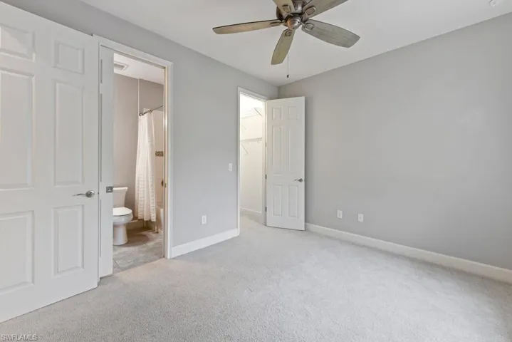 Unfurnished bedroom with a spacious closet, a closet, ensuite bathroom, light colored carpet, and ceiling fan