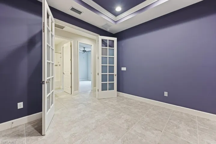 Empty room featuring a tray ceiling, ceiling fan, crown molding, and french doors