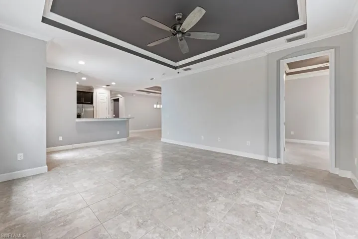 Unfurnished living room featuring crown molding, a raised ceiling, and ceiling fan