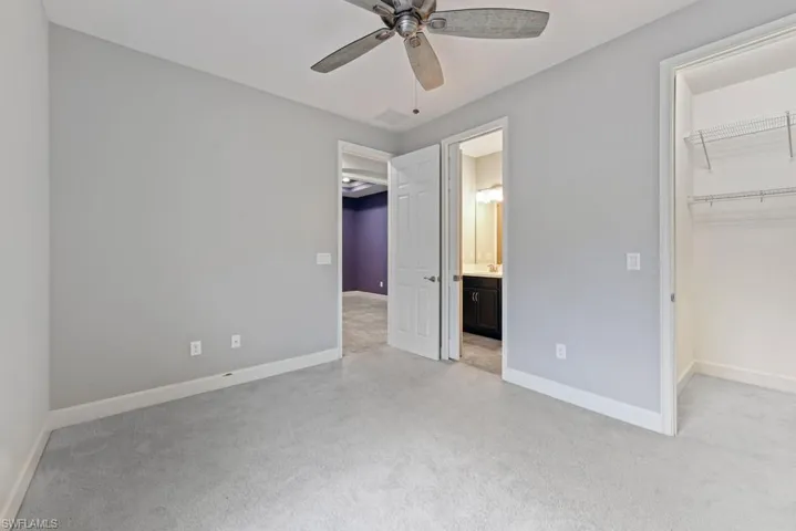 Unfurnished bedroom with a walk in closet, ceiling fan, and light colored carpet